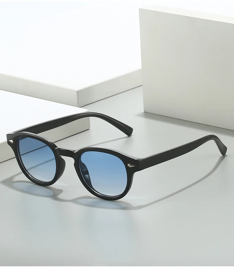 Lunettes de soleil noires modèle Azurea de la collection MILO avec monture épaisse en plastique et verres teintés bleu azur, dotées de petites décorations en forme de triangle métallique au niveau des charnières."